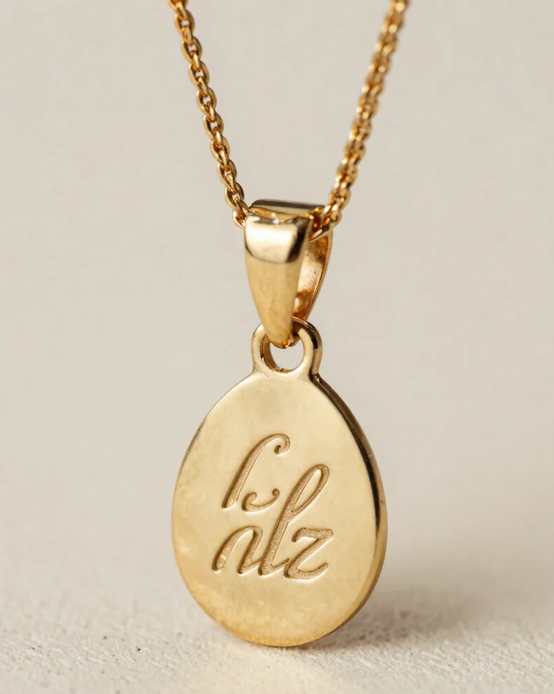 Macro studio photograph of a champagne gold pendant on an ivory backdrop, soft diffused light revealing fine engraved le