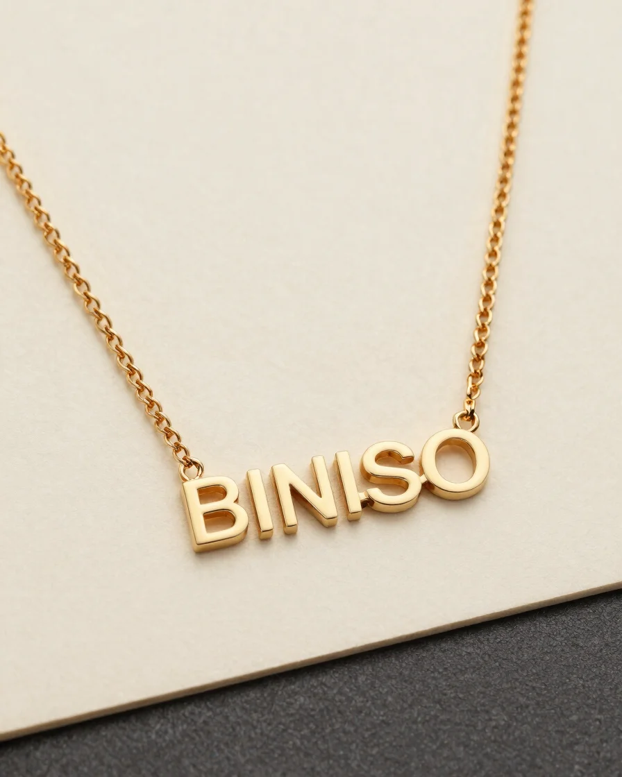 Macro product study of a champagne gold nameplate necklace on an ivory backdrop, soft diffused studio light revealing th
